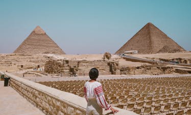 A tourist admires the Great Pyramids and Sphinx in Giza, Egypt under the clear daytime sky.